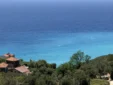 Red tile roofs of traditional houses nestled in the green hills above the bright blue ocean water in Lukovë