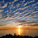 Golden evening sun reflecting on the calm ocean waters beneath a stunning cloud-filled sky in Lukovë, Albania.