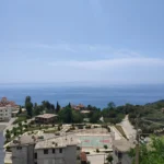 Elevated daytime view of the Lukovë village church, local sports court, and the clear blue sea horizon.