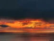 Dramatic fiery orange sunset and dark clouds over the ocean, seen from the elevated Kolagji Rooms.