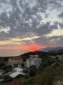 Elevated view of Lukovë village and the surrounding coastal mountains during a vibrant red ocean sunset.