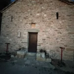 Front facade and wooden door of the historic stone church of Shën e Premte in Lukovë at dusk.
