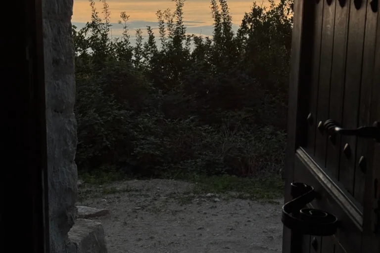 View looking out the open wooden door of Shën e Premte church towards a beautiful coastal sunset in Lukovë.