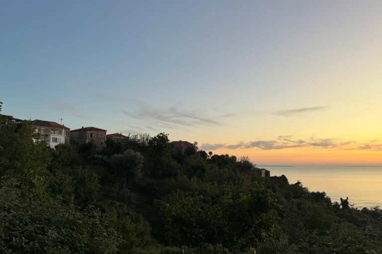 Historic stone houses on a hillside overlooking the sea at sunset near Shën e Premte in Lukovë.