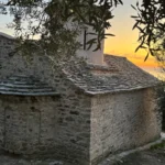 Traditional stone architecture and slate roof of the Shën e Premte church during a beautiful Lukovë sunset.