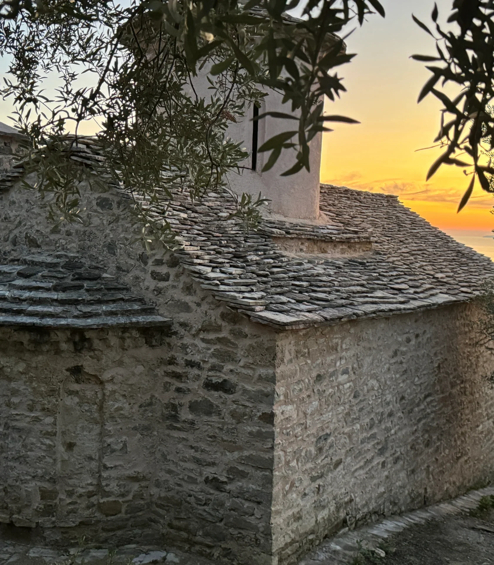 Traditional stone architecture and slate roof of the Shën e Premte church during a beautiful Lukovë sunset.
