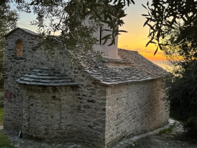 Traditional stone architecture and slate roof of the Shën e Premte church during a beautiful Lukovë sunset.