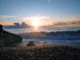 Ocean waves crashing against the shoreline rocks at Shpella Beach during a spectacular coastal sunset.