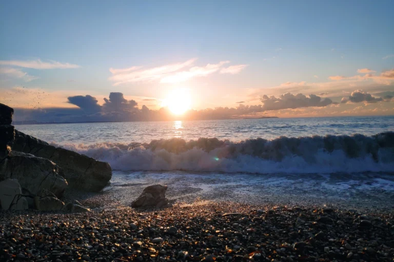 Ocean waves crashing against the shoreline rocks at Shpella Beach during a spectacular coastal sunset.