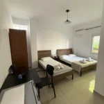 Spacious triple room layout featuring beds, a dining table, and natural light from the outdoor view window.