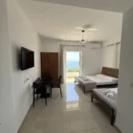 Spacious triple room with sea view balcony, dining table, and modern tile floors at Kolagji Rooms in Lukovë.