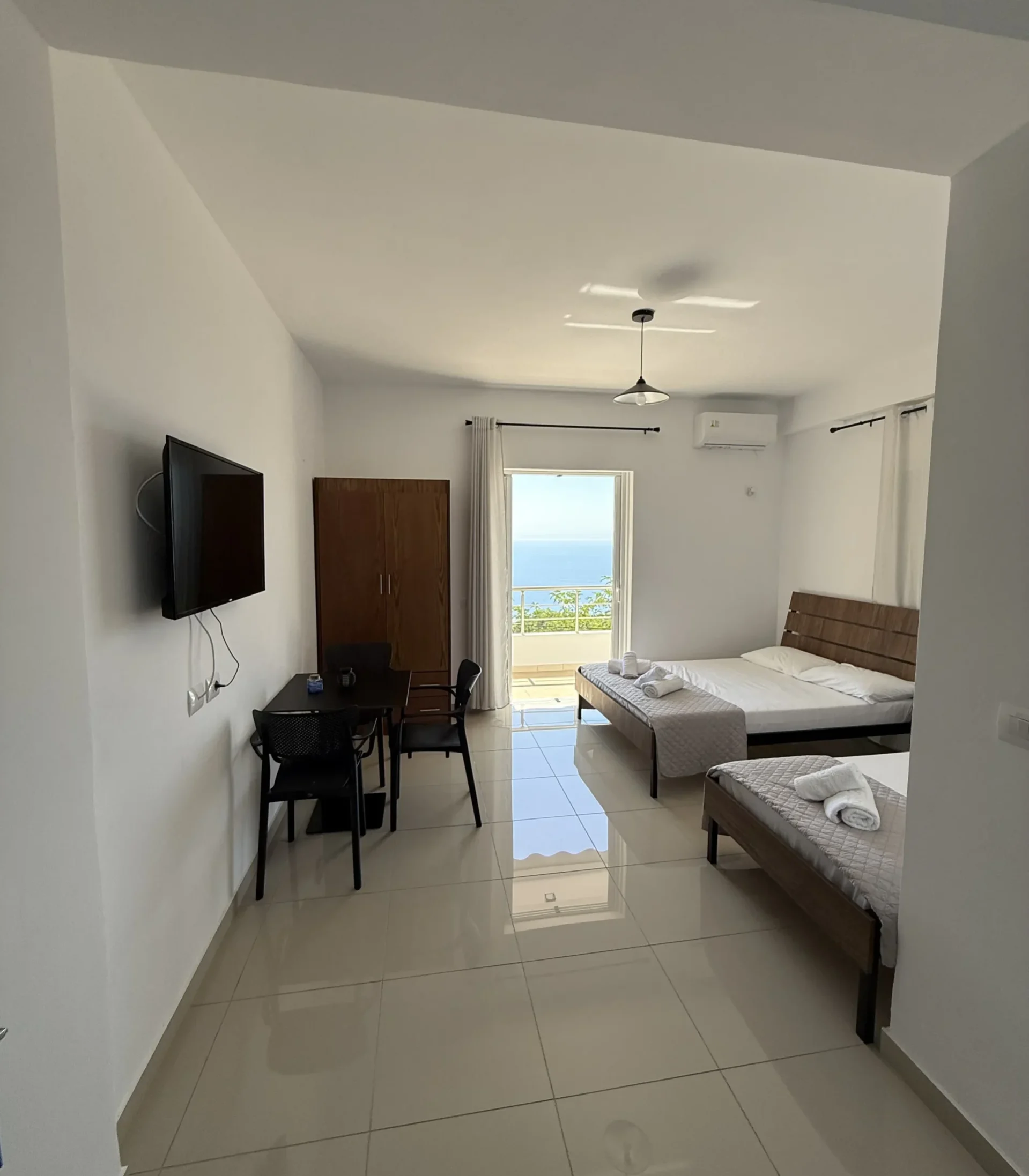 Spacious triple room with sea view balcony, dining table, and modern tile floors at Kolagji Rooms in Lukovë.