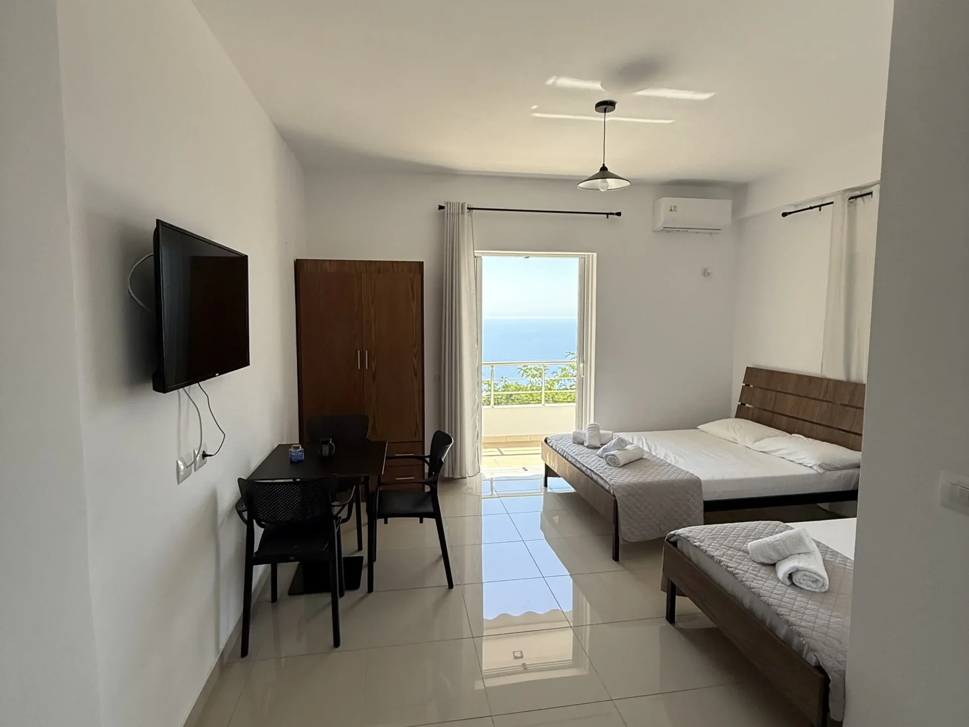 Spacious triple room with sea view balcony, dining table, and modern tile floors at Kolagji Rooms in Lukovë.