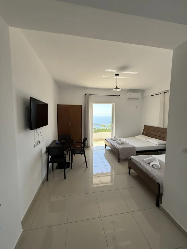 Spacious triple room with sea view balcony, dining table, and modern tile floors at Kolagji Rooms in Lukovë.