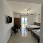 Flat-screen TV and dining area in the affordable Lukovë triple room, with doors opening to the Ionian Sea.