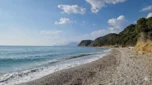 Gentle ocean waves washing onto the pebble shore of Lumra Beach with coastal mountains in the background in Lukovë.