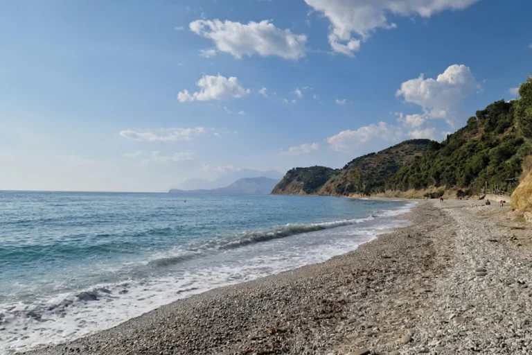 Lukova Beach 1 Gentle ocean waves washing onto the pebble shore of Lumra Beach with coastal mountains in the background in Lukovë.