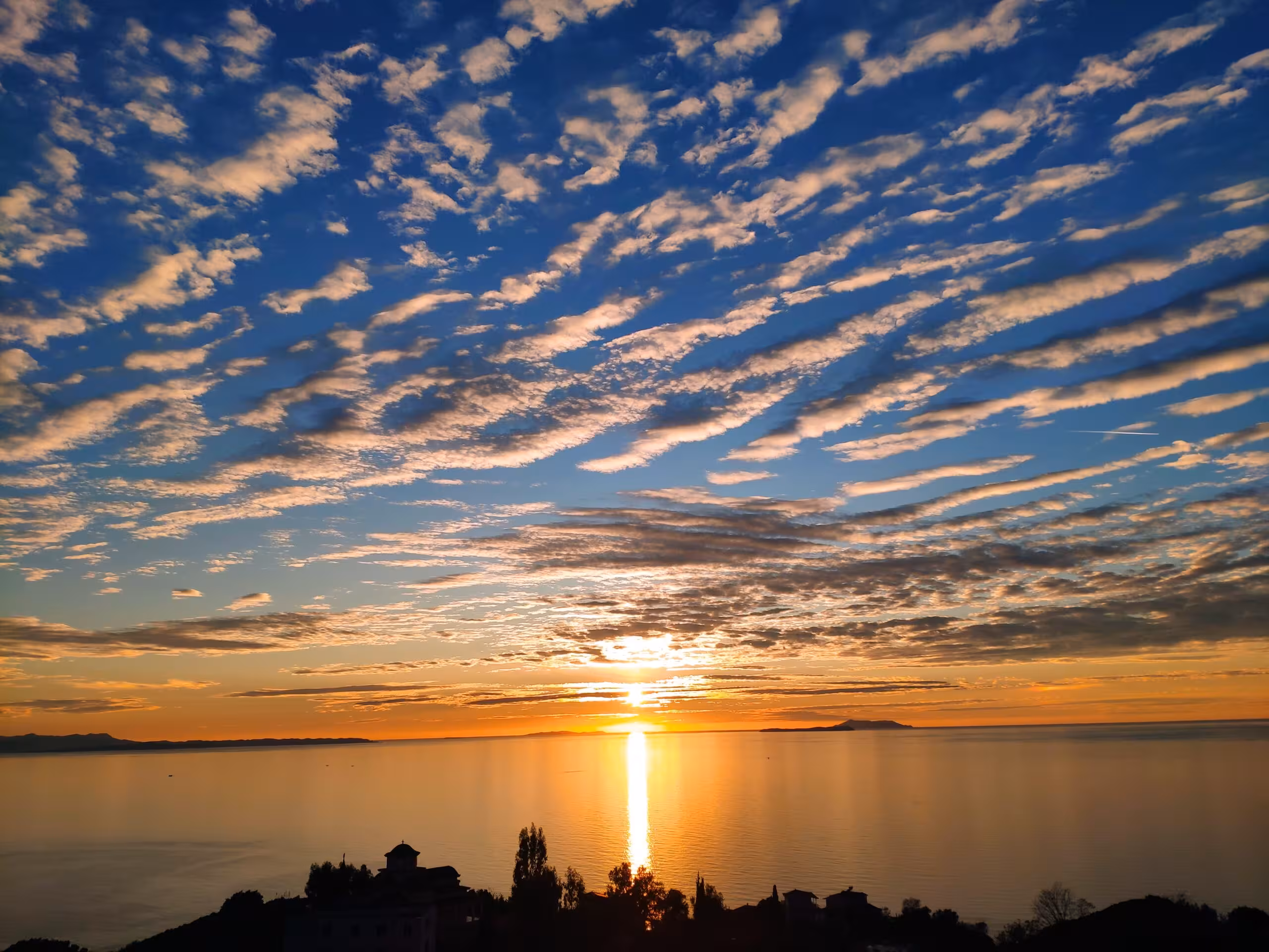Stunning evening sunset reflecting on the Ionian Sea beneath a sky filled with patterned clouds.