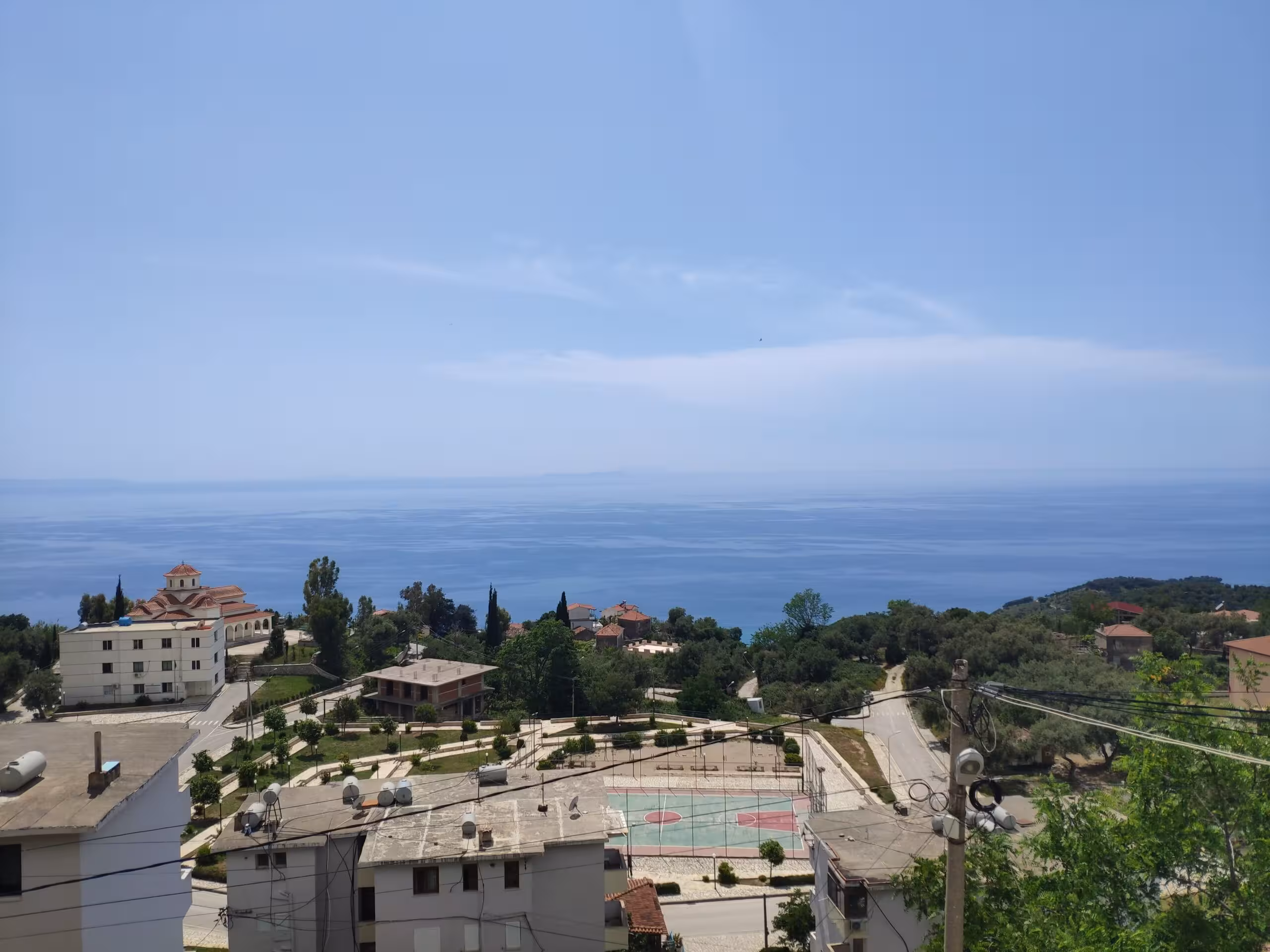 Panoramic daytime view of Lukovë village, the local sports court, and the expansive blue sea.